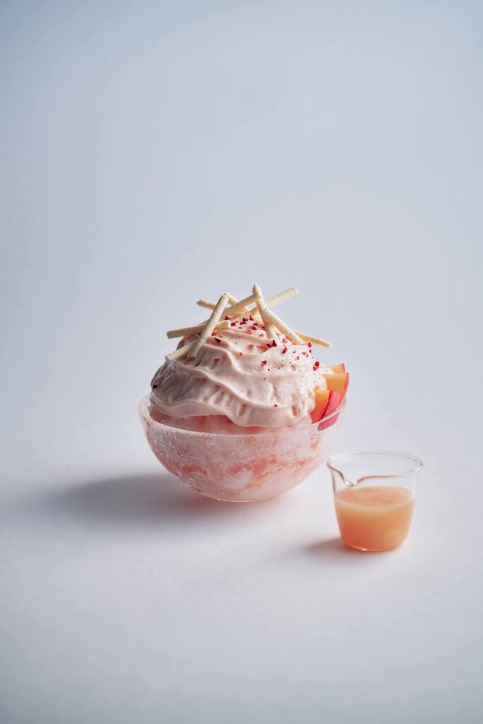 「AWA KO-RI　MOMO」は、極限まで薄く削ったきめ細やかな氷とケーキのパーツのように一つ一つ手間暇かけた具材を合わせ作り上げるモンサンクレールのかき氷「AWA KO-RI」。7月は桃とヨーグルトを合わせた酷暑にピッタリの爽やかな新作を販売。自家製の白桃ソースとヨーグルトソースを交互に重ね桃コンポートやフレッシュな果肉を合わせた。桃と練乳のエスプーマ、サクサクのメレンゲで仕上げている。
